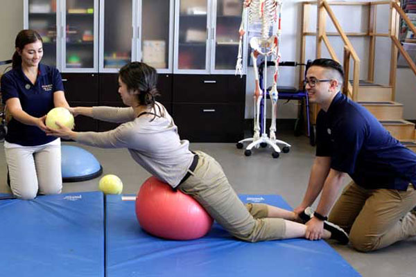three students on gym mat with medicine balls