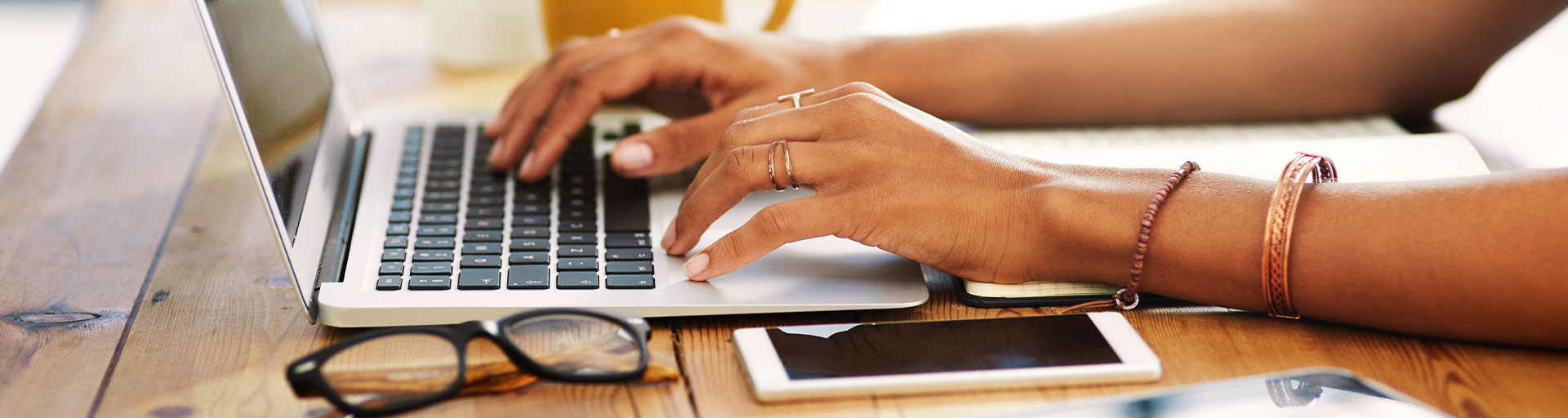 Hands typing on a laptop with smart phone next to it