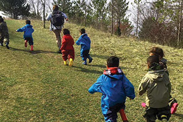 Group of toddlers dressed in rain attire running up a grassy hill