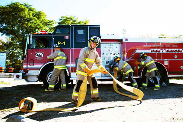 Four firefighters reeling hose of fire truck