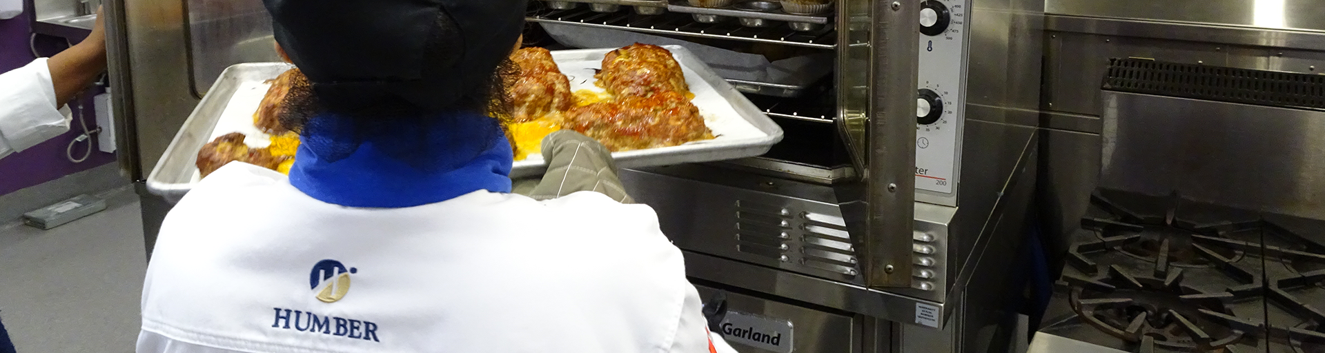 student pulling a sheet pan out of an oven