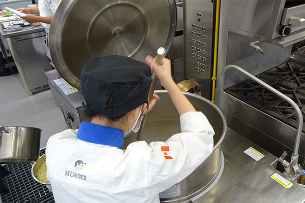 student stiring food in a large metal pot