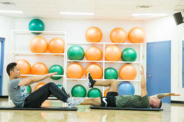 Two students in gym attire on their backs doing physical exercises