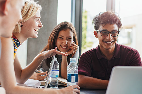 students sitting together at table with books and laptop