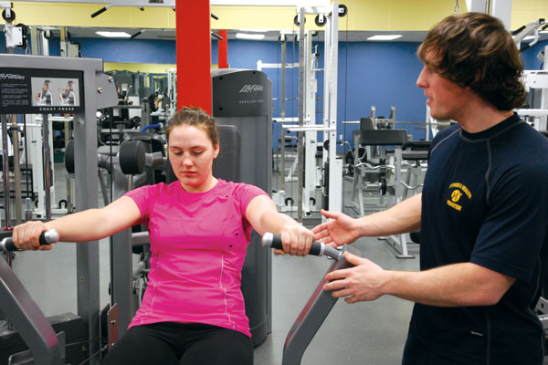 Fitness and health promotion student guiding someone on exercise equipment